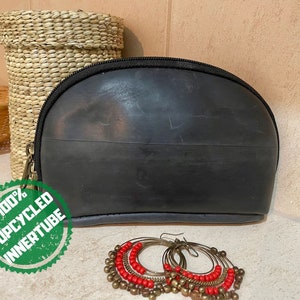 May include: Black, upcycled inner tube cosmetic bag with a zipper closure. The bag is next to a pair of hoop earrings with red beads and brass-colored accents. A green sticker reads "100% Upcycled Innertube".