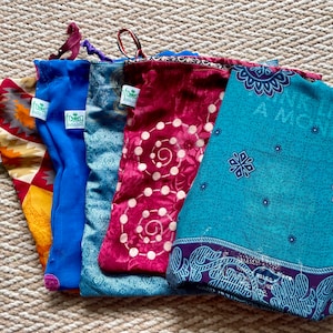 May include: Five reusable fabric bags with different patterns. The bags are blue, red, teal, and a multi-coloured pattern. The bags have a green leaf logo with the text "frog bags" on them.