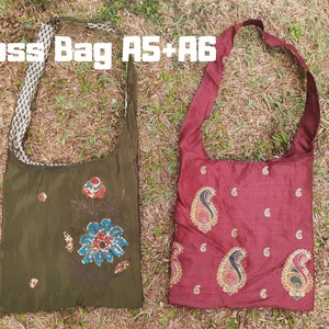 Pu&ograve; includere: Due borse a tracolla. Una &egrave; verde oliva con ricami floreali e un cinturino fantasia. L'altra &egrave; bordeaux con ricami paisley. Il testo "Cross Bag AS+A6" &egrave; in alto.