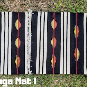 Pu&ograve; includere: Tappetino da yoga a strisce bianche e nere con disegni geometrici rossi, gialli e arancioni. Il tappetino ha frange alle estremit&agrave;. "Yoga Mat" &egrave; scritto in lettere nere nella parte inferiore dell'immagine.