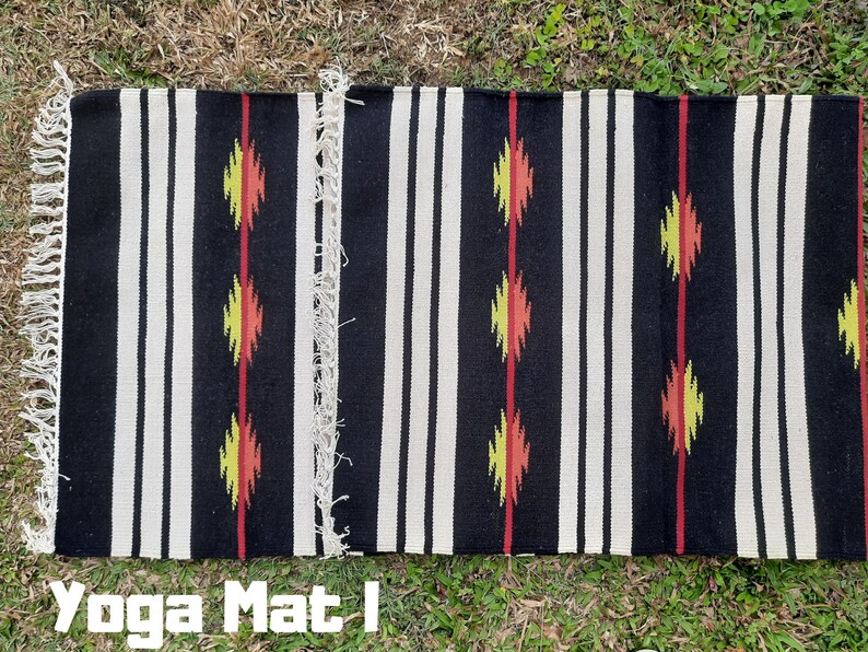 Pu&ograve; includere: Tappetino da yoga a strisce bianche e nere con disegni geometrici rossi, gialli e arancioni. Il tappetino ha frange alle estremit&agrave;. "Yoga Mat" &egrave; scritto in lettere nere nella parte inferiore dell'immagine.