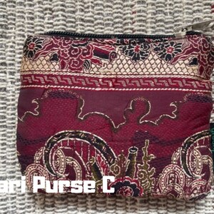 K&ouml;nnte beinhalten: Eine rote Stofftasche mit goldenen Mustern und einem Rei&szlig;verschluss. Die Tasche hat ein gr&uuml;nes Etikett mit dem Wort "greenswag" darauf. Die Tasche ist mit "Sari Purse C" beschriftet.