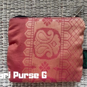 K&ouml;nnte beinhalten: Eine rote und goldene Sari-Tasche mit Rei&szlig;verschluss und einem gr&uuml;nen "greenliving"-Etikett. Die Tasche hat ein traditionelles indisches Design.