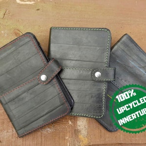 May include: Three black wallets crafted from upcycled inner tubes. The wallets feature red, green, and blue stitching. Each wallet has a snap closure. A green and white circular graphic reads "100% UPCYCLED INNERTUBES".