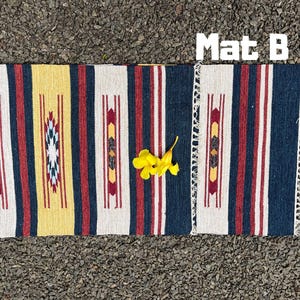 Pu&ograve; includere: Un tappeto tessuto con un motivo geometrico in tonalit&agrave; di giallo, rosso, bianco e blu. Il tappeto ha un bordo con frange ed &egrave; etichettato "Mat B".