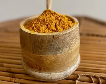Könnte beinhalten: Eine Holzschale gefüllt mit leuchtend gelbem Kurkumapulver. Die Schale hat eine natürliche Holzmaserung und eine hellbraune Farbe. Das Kurkuma ist fein gemahlen und hat einen leuchtenden, goldenen Farbton. Die Schale steht auf einer Bambusoberfläche.