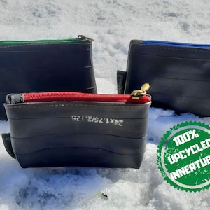 Op de afbeelding: Drie kleine ritszakjes gemaakt van gerecyclede binnenbanden. De zakjes zijn zwart met groene, blauwe en rode ritsen. De zakjes liggen op een wit besneeuwd oppervlak. Een groene cirkel met de tekst "100% UPCYCLED INNER TUBES" bevindt zich op de voorgrond.