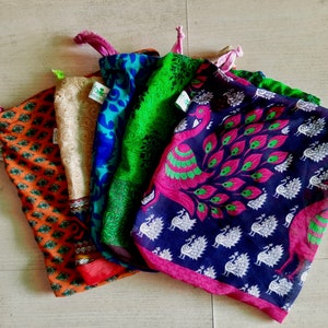 Könnte beinhalten: Fünf bunte wiederverwendbare Einkaufstaschen aus Stoff mit verschiedenen Mustern. Die Taschen sind gefaltet und übereinander gestapelt. Die oberste Tasche hat ein Pfauenmuster in Blautönen, Rosa und Grün. Die anderen Taschen haben florale und geometrische Muster in Orangetönen, Braun, Grün, Blau und Beige.