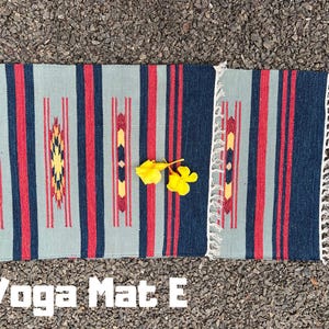 Pu&ograve; includere: Un tappetino da yoga a strisce blu, rosse e bianche con un bordo a frangia. Il testo "Yoga Mat E" &egrave; stampato sotto il tappetino.