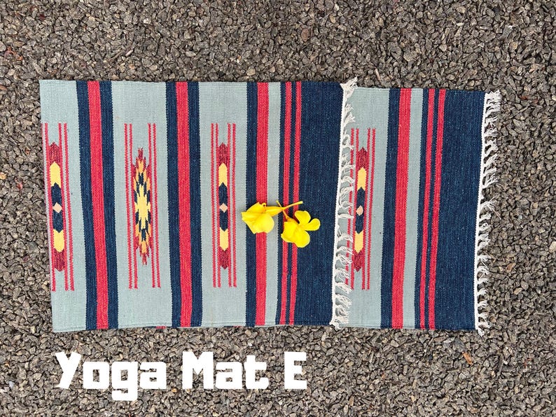 Pu&ograve; includere: Un tappetino da yoga a strisce blu, rosse e bianche con un bordo a frangia. Il testo "Yoga Mat E" &egrave; stampato sotto il tappetino.