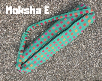 Pode incluir: Uma bolsa de tapete de ioga verde com fecho de correr e um design estampado de quadrados laranja e rosa. A bolsa tem uma alça longa para carregar no ombro. O texto "Moksha E" é visível no canto superior esquerdo da imagem.