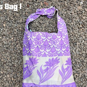 Pu&ograve; includere: Borsa a tracolla viola e bianca con un design floreale e paisley. La borsa ha una tracolla e il testo "Cross Bag I" nell'angolo in alto a sinistra. La borsa &egrave; in tessuto.