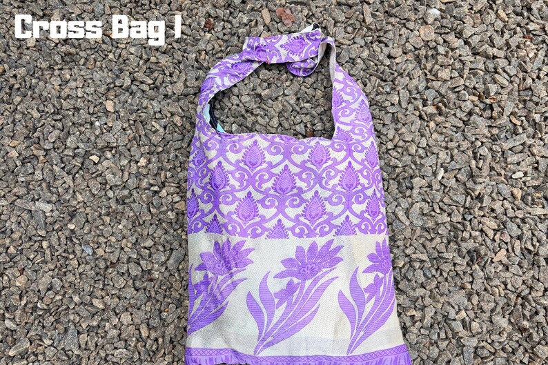 Pu&ograve; includere: Borsa a tracolla viola e bianca con un design floreale e paisley. La borsa ha una tracolla e il testo "Cross Bag I" nell'angolo in alto a sinistra. La borsa &egrave; in tessuto.