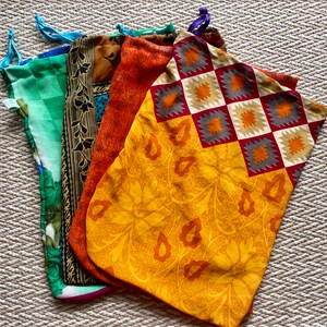 Pu&ograve; includere: Cinque sacchetti di stoffa con coulisse di diversi colori e motivi. I sacchetti sono realizzati con sari riciclati e sono perfetti per trasportare generi alimentari, articoli da toeletta o altri piccoli oggetti.