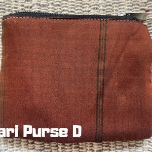 K&ouml;nnte beinhalten: Eine braune und gr&uuml;n gestreifte Stofftasche mit Rei&szlig;verschluss. Die Tasche hat ein gr&uuml;nes Etikett mit der Aufschrift "greenbag India Craft". Der Text "Sari Purse D" ist auf der Vorderseite der Tasche aufgedruckt.