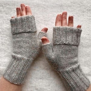 May include: A pair of gray fingerless gloves, knitted with a ribbed cuff and a textured stitch. The gloves are designed to cover the hand up to the knuckles, leaving the fingers free. The yarn has a subtle heathered effect, adding depth to the color.