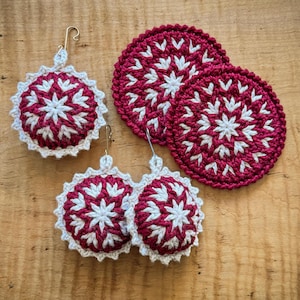 May include: A set of three round, crocheted items featuring a maroon and white starburst pattern with scalloped edges. One item includes a gold-toned metal hook for hanging, while the other two are flat, circular coasters.