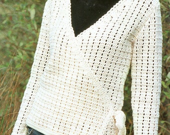 May include: A white crocheted wrap sweater with a V-neck and long sleeves. The sweater has a tie at the waist and is worn over a black turtleneck.