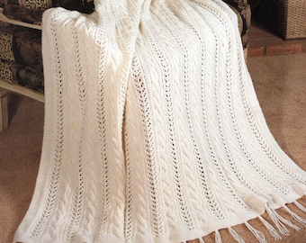 May include: A white knitted throw blanket with a cable knit pattern and fringe. The blanket is draped over a chair with a leopard print fabric.