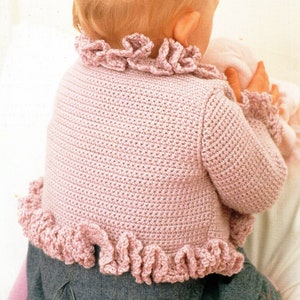 Puede incluir: Un cárdigan de bebé de color rosa tejido a crochet con ribetes de volantes alrededor del cuello y el dobladillo.
