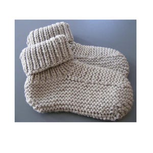 May include: A pair of beige knitted slippers with folded-over cuffs. The slippers are made with a thick yarn, showcasing a textured, chunky knit pattern. The cuffs are ribbed, adding a contrasting detail to the overall design. These cozy slippers are perfect for indoor wear.