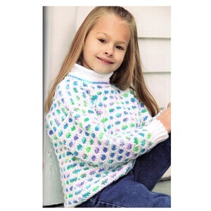 Könnte beinhalten: Ein weißer Pullover mit einem strukturierten Muster in Blau-, Grün- und Lilatönen. Der Pullover hat einen weißen Rollkragen und Bündchen. Die Person trägt eine blaue Jeans.
