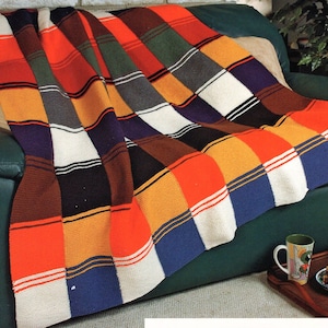 May include: A colorful knitted throw blanket with a checkered pattern in shades of orange, red, yellow, blue, green, brown, black, and white. The blanket is draped over a green couch.