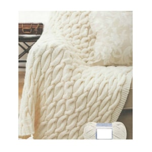 May include: A white cable knit throw blanket with a chunky knit texture. The blanket is draped over a couch and a ball of yarn is in the foreground.
