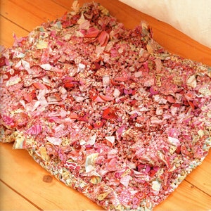 May include: A pink and white crocheted rug made from fabric scraps. The rug is made with a variety of different fabrics, including floral prints, stripes, and solids.