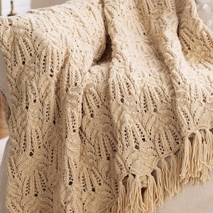 May include: A cream-colored knitted throw blanket with a lacy pattern and fringe trim. The blanket is draped over a chair.