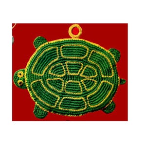Op de afbeelding: Een handgemaakte groene en gele gehaakte schildpadornament. De schildpad heeft een gedetailleerd schildpatroon en een lus om op te hangen. De achtergrond is effen rood.
