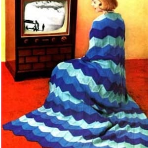 Peut inclure: Une femme est assise devant un téléviseur vêtue d'une couverture à motif chevron bleu et turquoise. La couverture est crocheté et présente un motif en zigzag.
