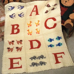 May include: Cream-colored, crocheted baby blanket featuring the alphabet. Each square displays a letter and a corresponding animal or object, such as ducks, cats, and elephants. The blanket has a scalloped edge and is designed with a classic, handmade aesthetic.