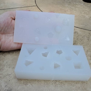 May include: Two white silicone molds for making resin crafts. The top mold has a variety of shapes including circles, triangles, and squares. The bottom mold has a variety of shapes including circles, triangles, and squares.