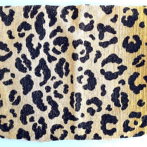 May include: A square textile cushion cover featuring a prominent black leopard print pattern set against a textured golden-tan background. The fabric displays a woven appearance with distinct dark spots distributed across the entire surface area.