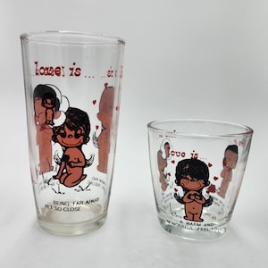 Pode incluir: Dois copos de vidro transparentes vintage com ilustrações de personagens de desenhos animados. Os copos têm as palavras "love is" e "being far apart yet so close" impressas. As ilustrações são em preto, vermelho e castanho.