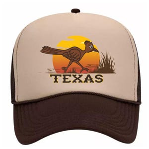 Può includere: Un cappello da camionista marrone e beige con un roadrunner dei cartoni animati e la parola "TEXAS" stampata sul davanti. Il roadrunner corre su uno sfondo di tramonto.
