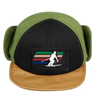 May include: A green and black fleece hat with ear flaps and a brown brim. The hat has a patch with a skier and a colorful stripe design.