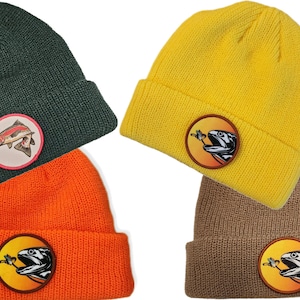 May include: Four knit beanies in different colors, each with a circular patch featuring a fish with a fly in its mouth. The beanies are green, yellow, orange, and brown.