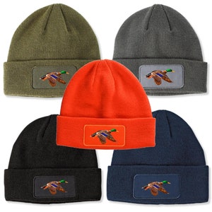 May include: Five different colored knit beanies with a patch of a mallard duck flying in a rectangle. The beanies are in the colors green, gray, orange, black, and navy blue.