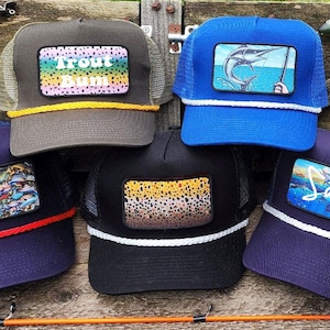 Può includere: Cinque diversi cappellini da camionista con varie toppe a tema pesca. I cappellini sono tutti blu navy, neri o verdi con bordino in corda bianca. Le toppe presentano immagini di pesci, un marlin e il testo "Trout Bum" e "Salty".
