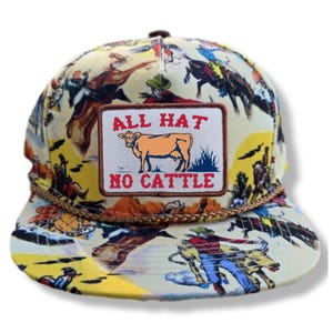 Könnte beinhalten: Gelbe und mehrfarbige Baseballkappe mit Cowboy-Motiv. Die Kappe hat einen Aufnäher mit einer Kuh-Illustration und dem Text "ALL HAT NO CATTLE". Die Kappe hat eine braune Seildetail um den Rand.