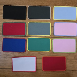 May include: Twelve rectangular fabric patches with different colored borders and backgrounds. The patches are arranged in three rows of four. The colors of the patches are black, dark green, light blue, red, gray, pink, blue, green, light pink, white, and red.