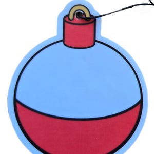 May include: A blue and red ornament-shaped air freshener with a black string for hanging. The ornament has a light blue upper section and a red lower section, separated by a black outline. The top section is red with a gold-colored loop.