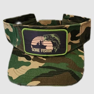 May include: Camouflage visor with a green border patch that says "Gone Fishin'" and a silhouette of a fish jumping out of the water with a sunset in the background.
