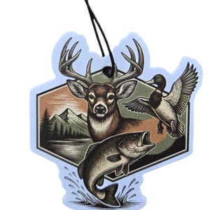 May include: A light blue air freshener with a hunting theme. The design features a deer, a duck in flight, and a fish leaping from the water. The background includes a mountain range and trees. A black string is attached for hanging.