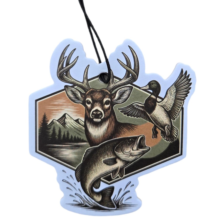 May include: A light blue air freshener with a hunting theme. The design features a deer, a duck in flight, and a fish leaping from the water. The background includes a mountain range and trees. A black string is attached for hanging.