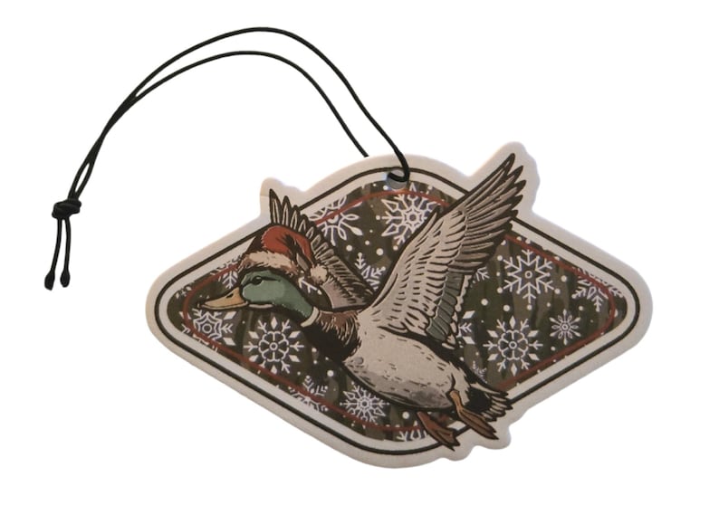 May include: A decorative air freshener featuring a flying duck wearing a Santa hat. The duck is depicted with detailed feathers and a green head. The background has a snowflake pattern. A black string is attached for hanging.