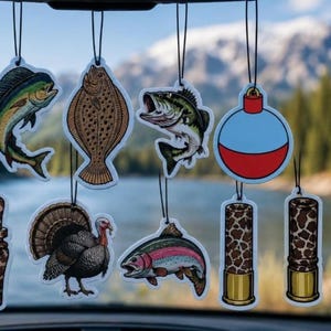 May include: A collection of hanging air fresheners featuring various outdoor designs including a mahi-mahi, a flatfish, a largemouth bass, a red and blue fishing bobber, a duck call, a wild turkey, a rainbow trout, and two shotgun shell casings.