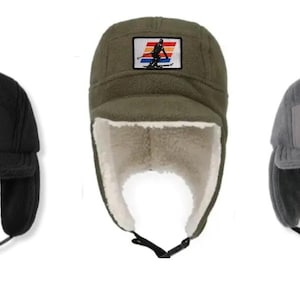 May include: Three fleece winter hats in black, olive green, and grey. Each hat features a rectangular patch with a skier graphic in front of a striped sunset design. The hats have ear flaps and chin straps.
